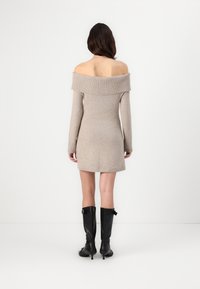 Μπεζ πλεκτό μίνι φόρεμα με ντεκολτέ τύπου off-shoulder και μακριά μανίκια. Φοριέται με μαύρες ψηλές μπότες με τακούνι. Λείος υφή.