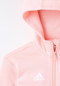 Ljusrosa Adidas hoodie med en mesh-fodrad huva, framzipper och vit logotyp. Mjuk tyg med slät yta och detaljerad sömnad.
