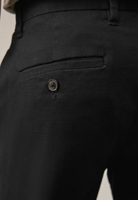 Pantaloni negri dintr-un material texturat, cu un buzunar aplicat și un detaliu cu nasture. Materialul pare durabil și neted.