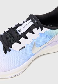 Light blue and black athletic shoe with textured upper, pronounced ridges, and a silver swoosh logo. Features black laces and a cushioned sole.