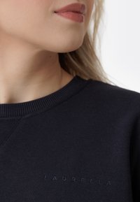 Felpa navy con colletto e polsini a costine. Presenta un logo "LAURELLA" in rilievo sul davanti. Texture liscia, design casual.
