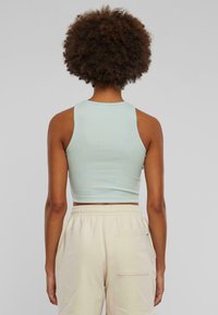 Light blue cropped tank top with a ribbed texture and wide straps, paired with cream-colored elastic waist pants featuring a back pocket.