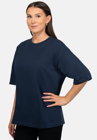 T-shirt en coton bleu marine avec des manches courtes, col rond, coupe décontractée et texture douce. Design légèrement surdimensionné.