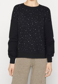 Sudadera negra hecha de tela suave, con acentos de piedras de strass dispersos, puños acanalados y un escote de cuello redondo. Ajuste casual y relajado.