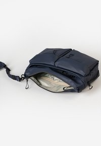 Donkerblauwe gevoerde schoudertas met twee externe zakken, ritsluiting en een ruime binnenkant met een lichtere, gestructureerde voering.