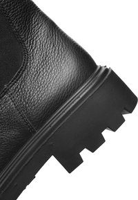 Sort læderstøvle med hæl, tekstureret overflade, tyk gummisål med dybt slidmønster og elastisk sidepanel.