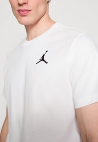 Fehér pamut póló, bal mellrészen fekete hímzett Jumpman logóval. A póló kerek nyakú és rövid ujjú.
