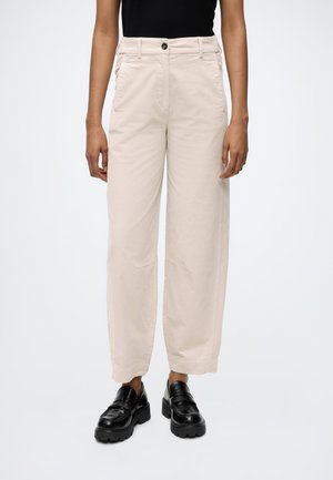 Persoon draagt beige wijde broek met hoge taille, zwarte plateau loafers en een zwart mouwloos topje tegen een effen achtergrond.
