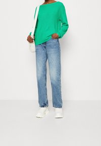 Grön ribbad tröja med vid halsringning, parat med blå raka jeans och klumpiga vita ankelstövlar, kompletterat med en liten vit väska.