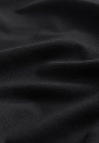 Juodas medvilninis audinys su lygiu paviršiumi, kuriame matyti švelnios raukšlės ir klostės, pabrėžiančios jo lengvumą ir lankstumą.