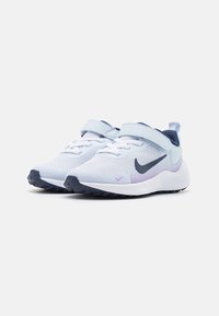 Dziecięce jasnoniebieskie i białe sneakersy Nike z granatowym logo, z zapięciem na rzep i czarną teksturowaną podeszwą, pod kątem w widoku z przodu.