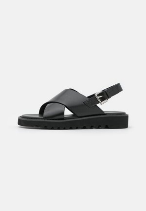 Schwarze Leder-Sandalen mit einem Kreuzriemen-Design, verstellbarem Schnallenverschluss und strukturierten Sohlen mit Rippen für besseren Halt.