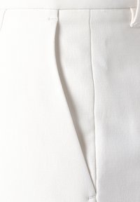Tessuto bianco con una superficie liscia, caratterizzato da una cucitura verticale e tasche inclinate, progettato per pantaloni strutturati.
