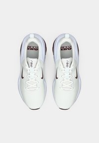 Λευκά αθλητικά παπούτσια Nike με μπορντό λεπτομέρειες. Διαπνοίον πλέγμα στην άνω πλευρά, στρογγυλή μύτη, επίπεδα κορδόνια, μαξιλαρωτή σόλα. Το λογότυπο "Air Zoom" είναι ορατό στο εσωτερικό.