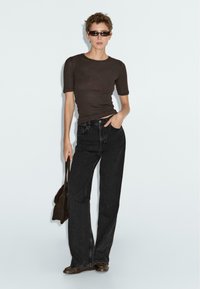 Brown fitted short-sleeve top paired with high-waisted black wide-leg jeans. Accessories include small black sunglasses and a brown shoulder bag.