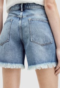 Shorts de mezclilla azul claro con dobladillo deshilachado, con talle medio y dos bolsillos traseros. La tela tiene una textura desteñida.