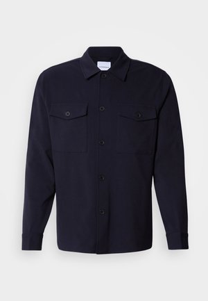 Navy blue shirt jacket made of soft fabric, featuring two chest pockets, a button-down front, and long sleeves with buttoned cuffs.