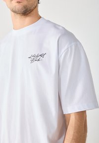Valge puuvillane T-särk lühikeste varrukatega, ümmarguse kaelusega, millel on musta kalligraafiatüüpi logo "Key West Beach" vasakul rindkeres. Pehme tekstuur.