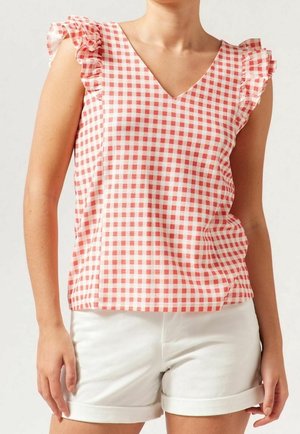 Kobieta ubrana w czerwoną i białą, bezrękawnikową bluzkę w kratkę z falbankami, zestawioną z białymi, podwiniętymi szortami, widoczna od szyi do połowy uda.