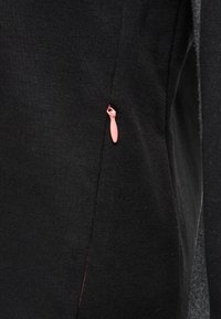 Tessuto a maglia nero con una tasca zip prominente dotata di un cursore rosa. Il design presenta linee pulite e una texture liscia.