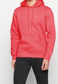 Sudadera color coral con un bolsillo frontal, capucha con cordón y logotipo bordado. Tejido suave con puños y dobladillo acanalados.