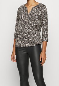 Schwarze Bluse mit V-Ausschnitt, dreiviertel Ärmeln und kleinen floralem Muster in Creme und Rot. Weicher Stoff mit lässigem Schnitt.