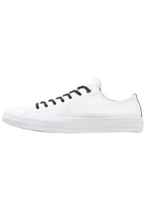 Witte lage canvas sneaker met zwarte veters en witte rubberen zool, getoond vanaf de binnenkant op een witte achtergrond.