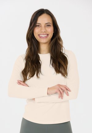 Langarm lichtbeige top met een gladde textuur, ronde halslijn en aansluitend ontwerp. Het model staat met de armen gekruist en toont de shirt.