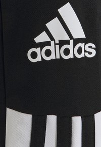 Tela negra con el logo blanco de Adidas encima de franjas verticales en blanco y negro, mostrando la textura del material.