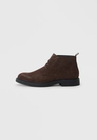 Botas de tobillo de ante marrón con una textura suave, presentando un diseño con cordones, punta redonda y una suela de goma negra.