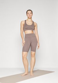 Brown athletic crop top and matching high-waisted shorts. The material appears smooth with a fitted design, suitable for activewear.