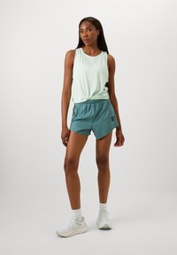 Light green sleeveless top paired with teal shorts. Sneakers are white with mint accents. Smooth fabric and relaxed fit throughout.