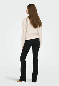 Lichtbeige langärmige top met een gerimpelde zoom, gecombineerd met strakke zwarte flare jeans en nude puntige hakken. Eenvoudig, strak ontwerp.