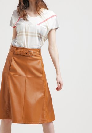 Vrouw draagt een wit topje met korte mouwen met rode en beige strepen en een A-lijnrok van hoog getailleerd bruin leer met ceintuur.