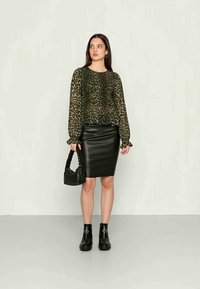 Blusa com estampa de leopardo em tecido verde transparente, saia lápis de couro preta, botas chunky pretas, bolsa trançada. Corte justo, mangas longas.
