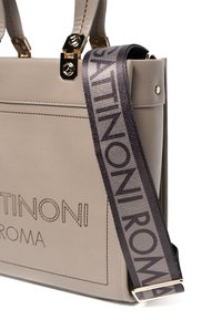 Beige leren handtas met gouden accenten, voorzien van een logo in donkerbruin. Inclusief een afneembare grijze schouderband met herhaald merklogo.