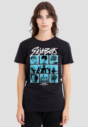 Young woman wearing black T-shirt with blue cartoon-style portraits and silhouettes, white stylized text "SAJABOYS," and "KPOP DEMON HUNTERS" below.