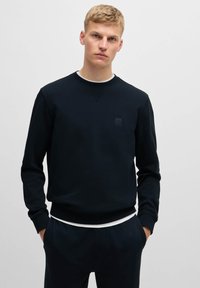 Granatowy sweter z okrągłym dekoltem, z teksturowaną łatą na klatce piersiowej, ściągaczami przy mankietach i u dołu, wykonany z miękkiej bawełny, łączącej komfort z trwałością.