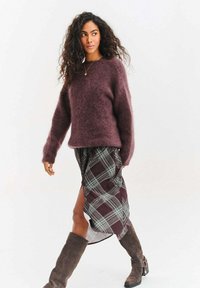 Bordowy, miękki sweter, spódnica w kratę z ciemnoczerwonym, niebieskim i białym wzorem, brązowe kozaki do kolan, gładka tekstura, luźny krój.