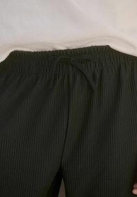 Czarne, prążkowane spodnie z elastycznym paskiem w talii i sznurkiem. Materiał wydaje się miękki i ma pionową teksturę. Część jasnego topu jest widoczna powyżej.
