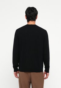 Black knit sweater with long sleeves, round neckline, and relaxed fit. Smooth texture with a solid color and subtle hem detailing at the bottom.