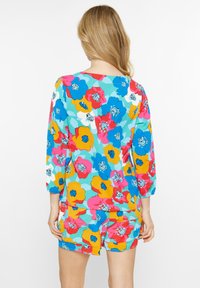 Blomstermønstret jumpsuit i livlige farver som pink, blå, gul og grøn, med trekvartærmer og en afslappet pasform.