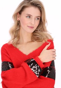 Rode trui met een V-hals en lange mouwen. Heeft een gestructureerde gebreide stof en zwarte paillettenaccenten op de mouwen. Zacht, pluizige textuur.