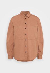 Camicetta color ruggine realizzata in un tessuto morbido, con colletto, maniche lunghe, chiusura con bottoni e due tasche sul petto.