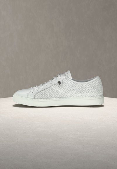 Baskets basses blanches avec un design en cuir tressé, avant à lacets et détail logo argenté sur un fond neutre.