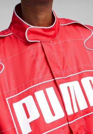 Gros plan d'une personne portant une combinaison de course rouge avec des coutures blanches et un grand logo Puma blanc sur la poitrine.