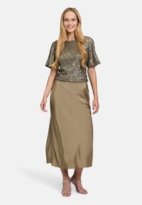 Glitzerndes Top in Gold mit kurzen schwingenden Ärmeln; kombiniert mit einem fließenden, olivgrünen Satinrock; Model trägt silberne Riemchen-Highheels.