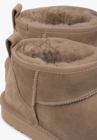 Para beżowych zamszowych botków za kostkę z grubą wełnianą podszewką oraz detalami przeszyć po bokach i z tyłu z pętlami do wsuwania.