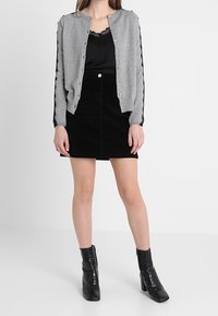 Grå stickad cardigan med knappstängning, matchad med en svart topp och svart mocka mini kjol. Svarta ankellång skor fulländar outfiten.