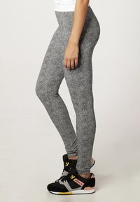 Svarta och vita mönstrade leggings med en figurnära design, slät textur och hög midja. Tillsammans med svarta och rosa träningsskor.